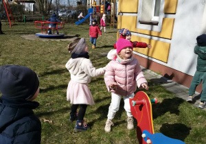 Widok na grupę bawiących się w ogrodzie przedszkolnym dzieci, które łapią spadające bańki mydlane.